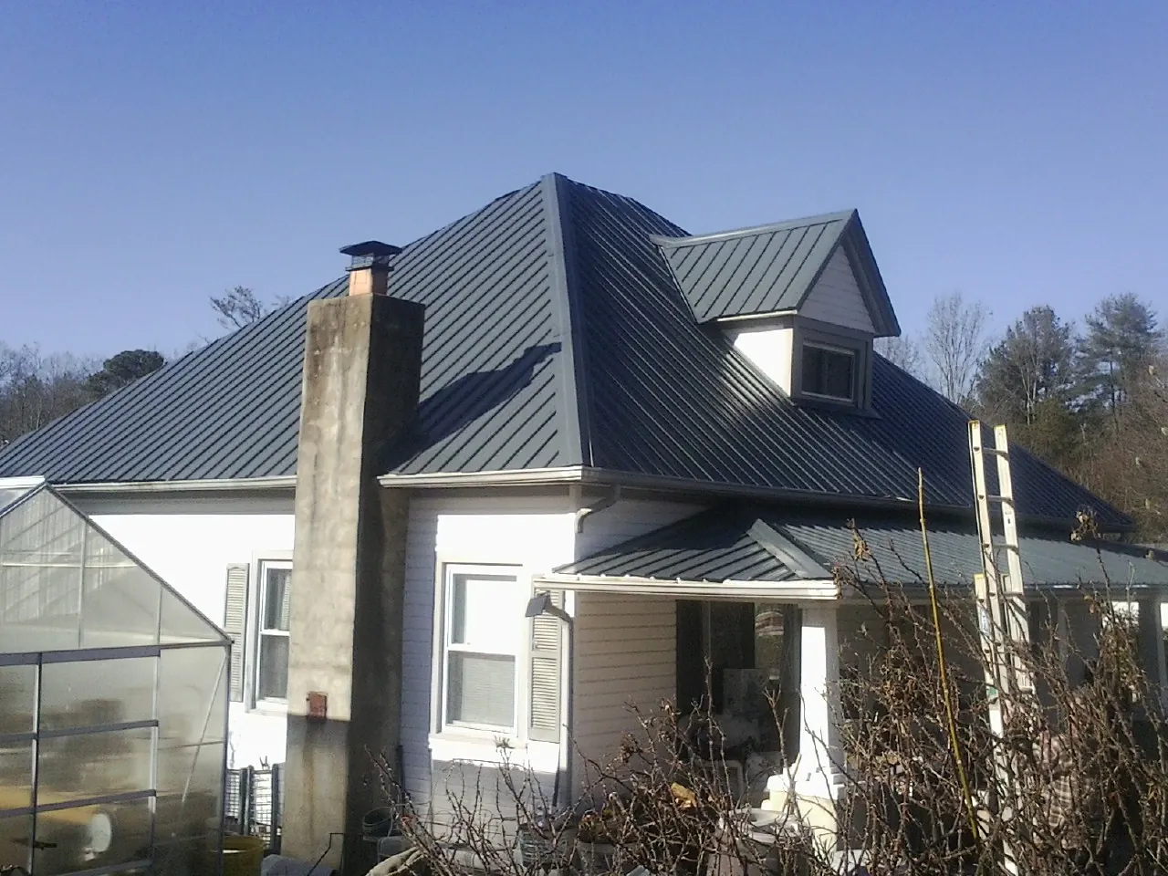 Dark blue standing seam metal roof on a white farmhouse with dormer — Slate & Tile Roof Repair by Roofing Brothers in Kingwood