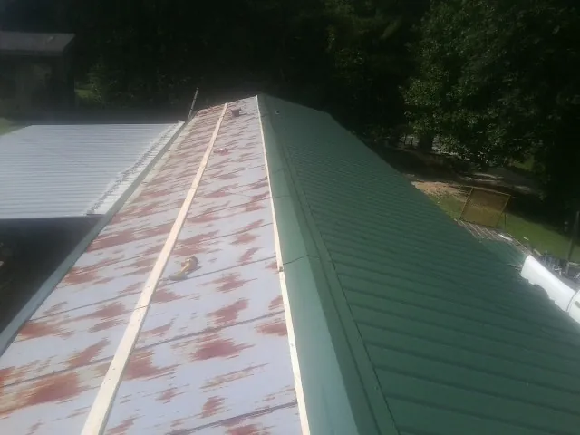 Old rusted panels beside newly installed green metal roofing — Wind Damage Roof Repair by Roofing Brothers in Kingwood