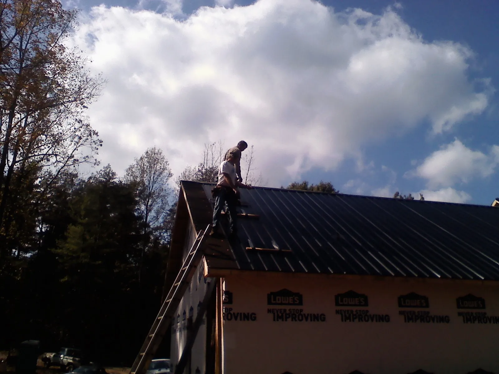 Roofer fastening dark metal panels high against a cloudy sky, from a Roof Inspection job in Kingwood