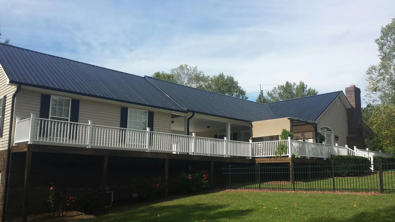 Black metal roof above a long white railed deck on a hillside home in Kingwood